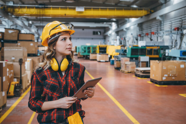 Portrait of young female industry worker with digital tablet in a factory Young maintenance engineer woman in protective clothing using touchpad with digital tablet