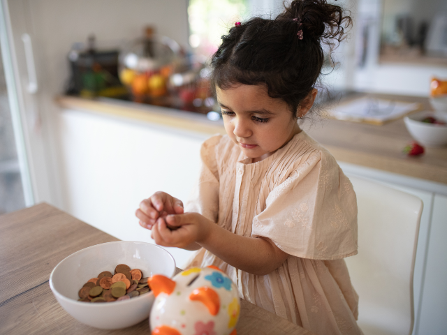GettyImages-1405574452 Little multiracial girl saving her money in to porcelain pig.