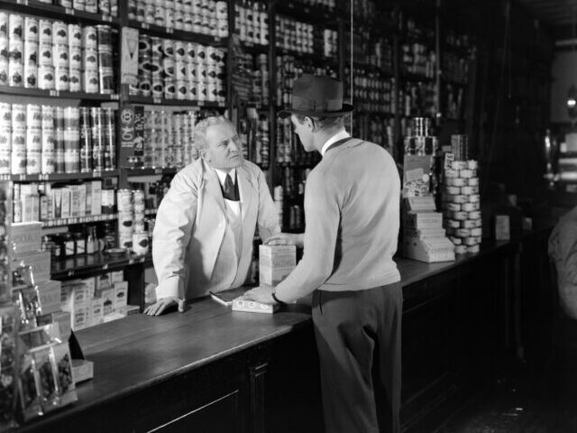 1930s 1940s TWO MEN... 1930s 1940s TWO MEN CUSTOMER AND CLERK IN GENERAL STORE TALKING OVER COUNTER (Photo by H.