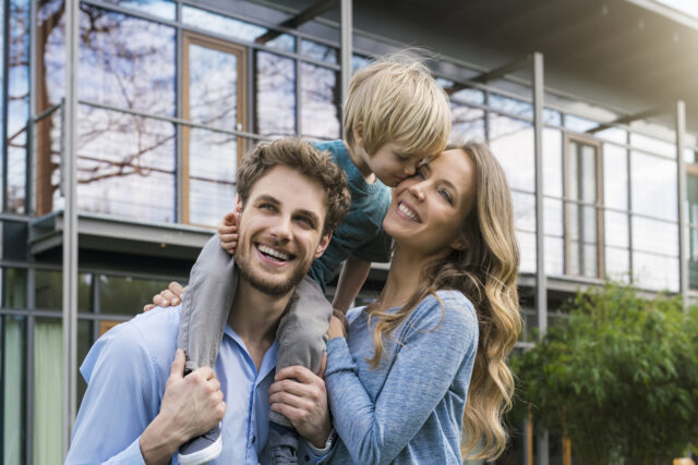 Happy parents with son in front of their home Germany, portrait of smiling family of father, mother and cute toddler boy standing in gar