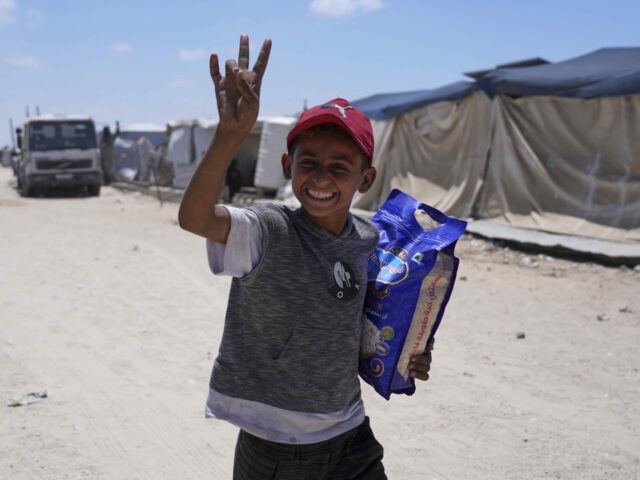 GHF Day 2 (Abdel Kareem Hana / Associated Press) A Palestinian child smiles to the camera as carries a bag of rice delivered by the U.S.-ba