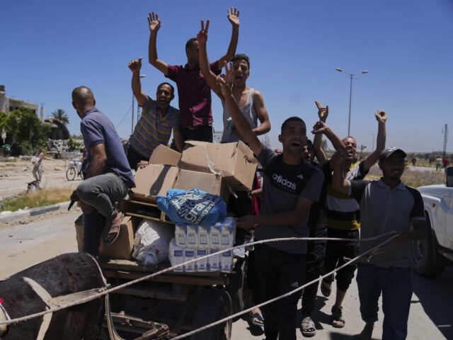 Palestinians GHF aid (Abdel Kareem Hana / Associated Press) Palestinians wave to the camera as they carry boxes and bags containing food and humanitar