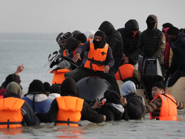 gettyimages-2217460092-1-640x480-1 People thought to be migrants wade through the sea to board a small boat leaving the beach