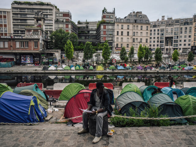 gettyimages-967047222-1-640x480-1 TOPSHOT - A man sits as migrants prepare their belongings at the start of the evacuation b
