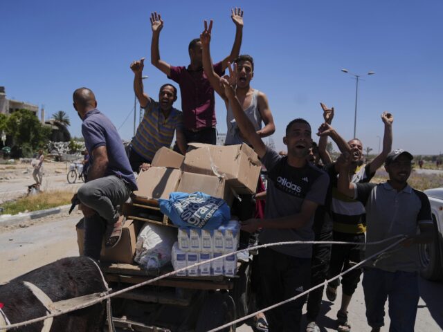 GHF (Abdel Kareem Hana / Associated Press) Palestinians wave to the camera as they carry boxes and bags containing food and humanitar