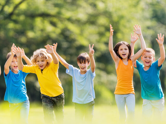 Happy children running outdoors Large group of cheerful boys and girls running in nature with their hands raised.