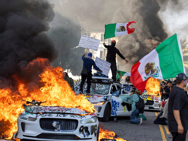 los-angeles-ice-protest-burning-cars-mexican-flags-jun8-25-getty Demonstrators wave flags from atop a wrecked car, standing beside burning Waymo vehicles,