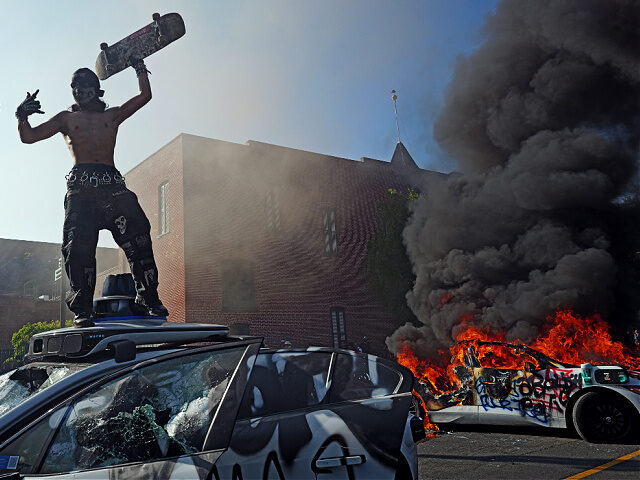 LOS ANGELES, CALIFORNIA - June 09: A protestor stands on a vandalized Waymo car during a p