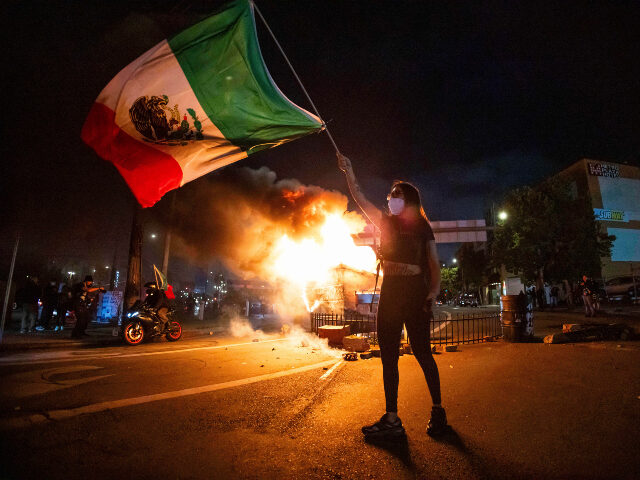 Los Angeles riots Mexican flag A woman waves the Mexican flag as flames erupt from a burning dumpster during a protest in