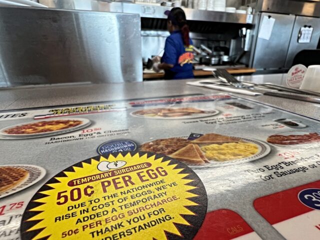 A menu in a Waffle House restaurant displays a sticker advising customers of a 50 cent pri